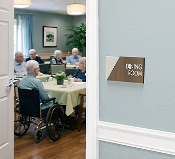 An Incline room sign labels a nursing home dining room where residents are gathered to socialize over a meal.