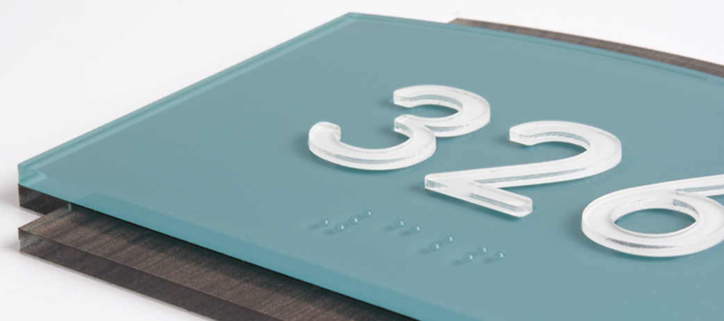 A room identification sign showing tactile text, braille, and a high-contrast room number.