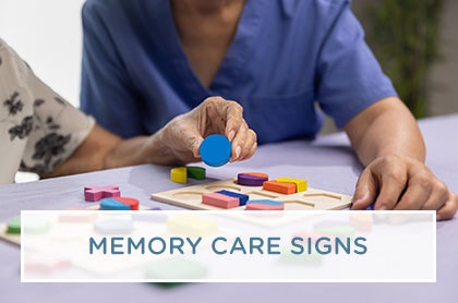 A caregiver provides gentle, cognitive assistance to a resident in a memory care wing of a senior care facility.