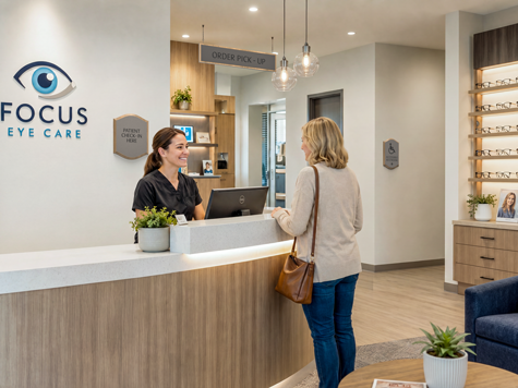 A modern vision center front desk with Town Square check-in signage, an order pickup sign, and a patient reception area.