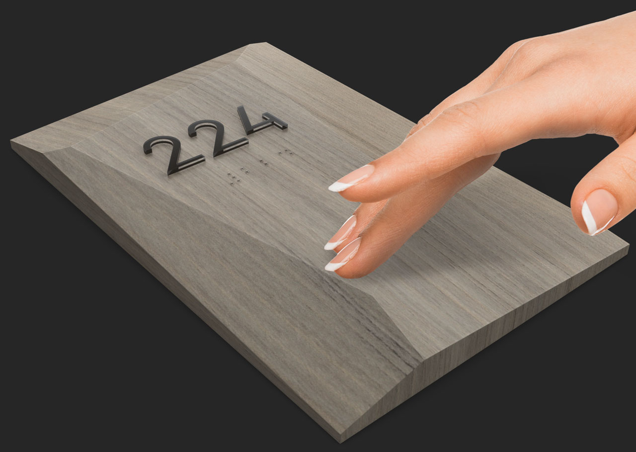 A hand feeling the surface finish of a Facets room number sign.