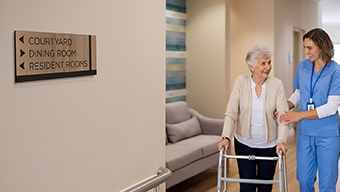 A nurse assists a rehab patient with a walker. Clear wayfinding help ensure patients can navigate independently as rehabilitation progresses.