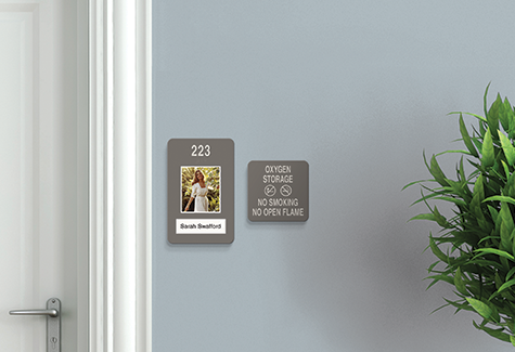 A resident walks through a modern senior care corridor with clear room identification and accessible wayfinding signs.