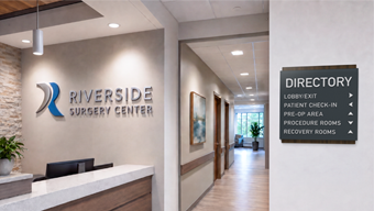 An outpatient surgery center corridor with a directory sign pointing to patient check-in, procedure areas, and recovery spaces.