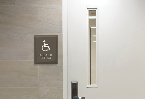 A resident walks through a modern senior care corridor with clear room identification and accessible wayfinding signs.