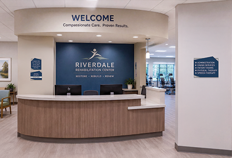 A resident walks through a modern senior care corridor with clear room identification and accessible wayfinding signs.